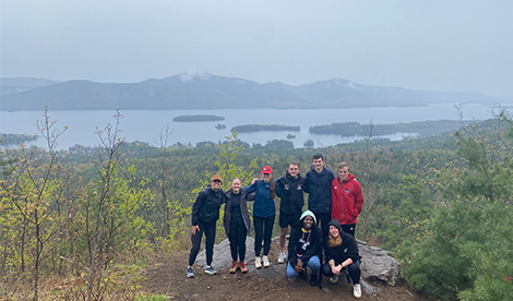 A group of students smiles in front of lake