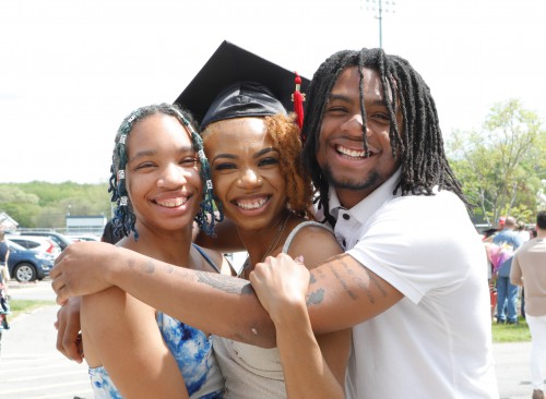 A woman and man hug a woman in a grad cap. They all smile widely.