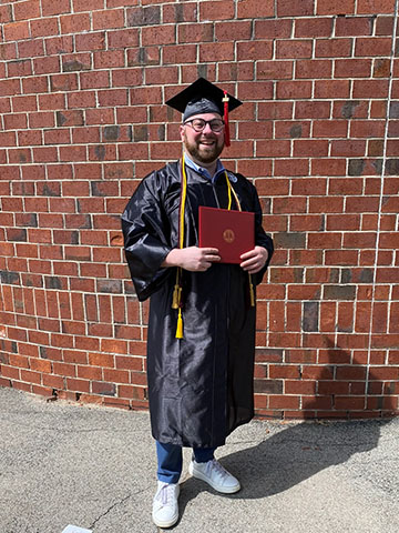 Alexander smiles whlie holding his diploma at commencement