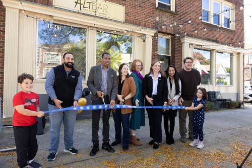 A group of people cuts a ribbon in front of a storefront