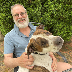 Anthony Petrillo holds a big dog on his lap and smiles.