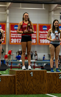 Brynn stands on podum and holds trophy while smiling.