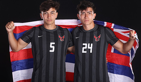 Two young men wearing Roberts soccer uniforms hold the Hawaiian flag behind them.