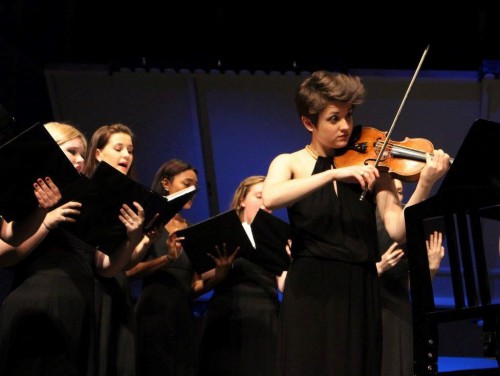 Becca playing violin in front of a group of students singing.