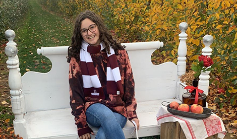 Chloe, a young woman, sits on a white bench outside and smiles.