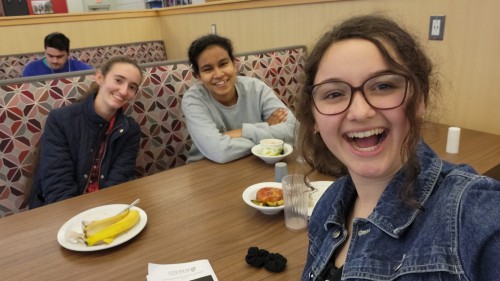 3 student sit at a booth table in the Garlock dining hall with food in front of them. They smile while taking a selfie.