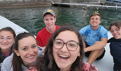 6 students sit on a dock and smile.