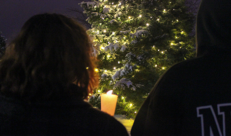 2 people's backs. Between them you can see a tree covered in snow and lights.