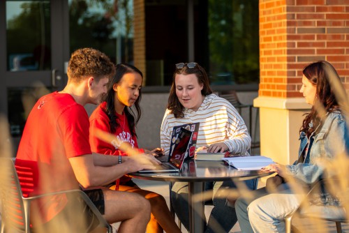 4 student sit around a circular table outside and do schoolwork.