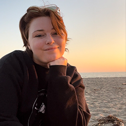 A young woman smiles slightly in front of a sunset.