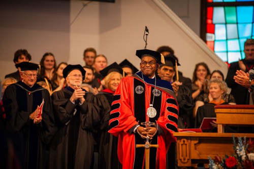 President Hayles smiles on stage and board members clap behind him.