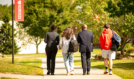 4 people walk facing away from the camera, including 3 students and President Hayles.