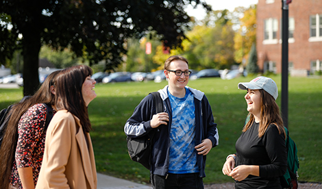 Four studnets stand outside on campus and laugh and smile together.