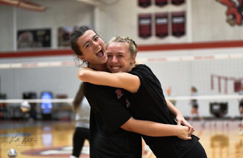 Holly and Jaycee smile and hug on a volleyball court