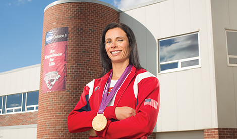 Jenn Suhr smiles in front of the Voller Athletic Center with an Olympic medal.