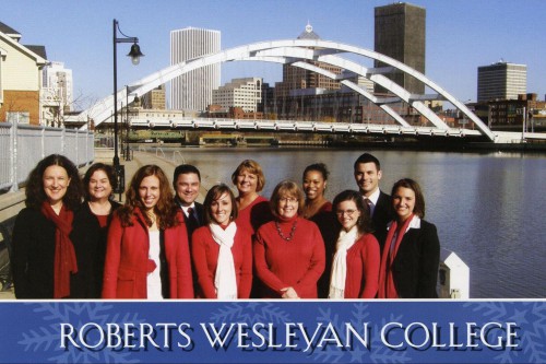 A group of people smiles in front of water and bridge in downtown Rochester