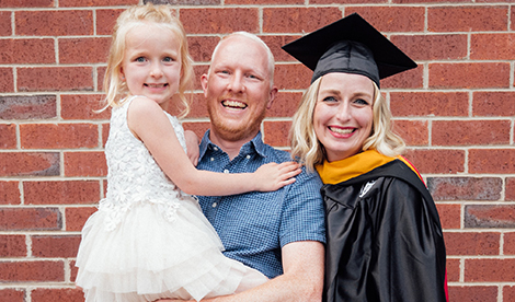 Kristen in her graduation gown and cap, smililng with a man and young child