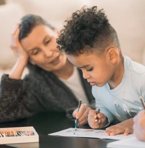 A woman and young boy draw in a coloring book together.