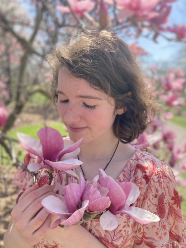 Lydia holds and looks down at a pink flower