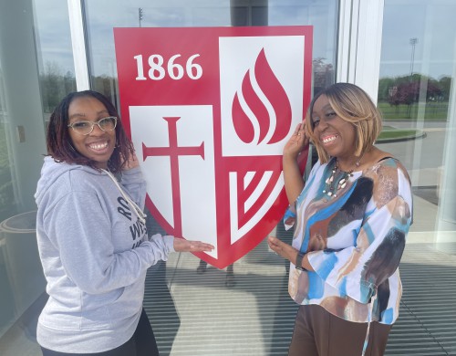 Jaylah and Melinda smile in front of Roberts shield.