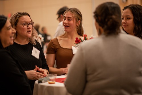 Students mingle around a table with some professionals. One speaks.