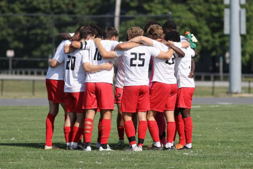 Men's soccer team huddles on the field.