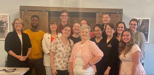 A group of 14 people, spanning in age, stand and smile.