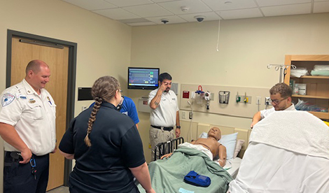 A group of various different healthcare workers stand around a mannequin patient in the simulation center