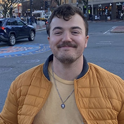 A young man stands and smiles in front of a city street.