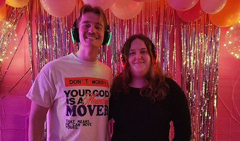 A young man and woman smile in front of balloons.