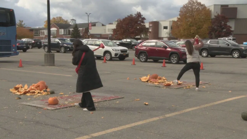 2 people smash pumpkins in a parking lot.