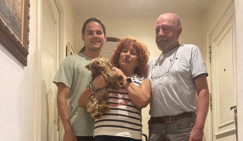 A young man, woman holding a dog, and man stand.