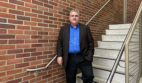 Steven stands on stairs in front of a brick wall and smiles.