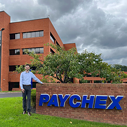 Timothy 
Bovee stands and smiles next to Paychex sign