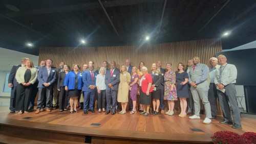 A large group of people smile on stage.