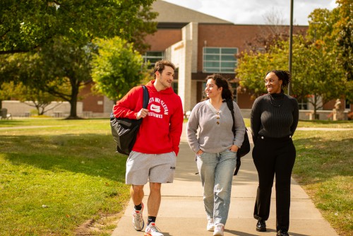 3 students walk on campus and talk to each other.