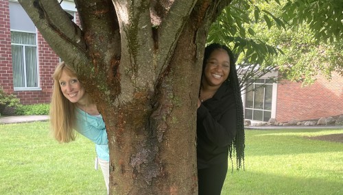 Wendy and Mya smile whle peeking their heads out from behind a tree