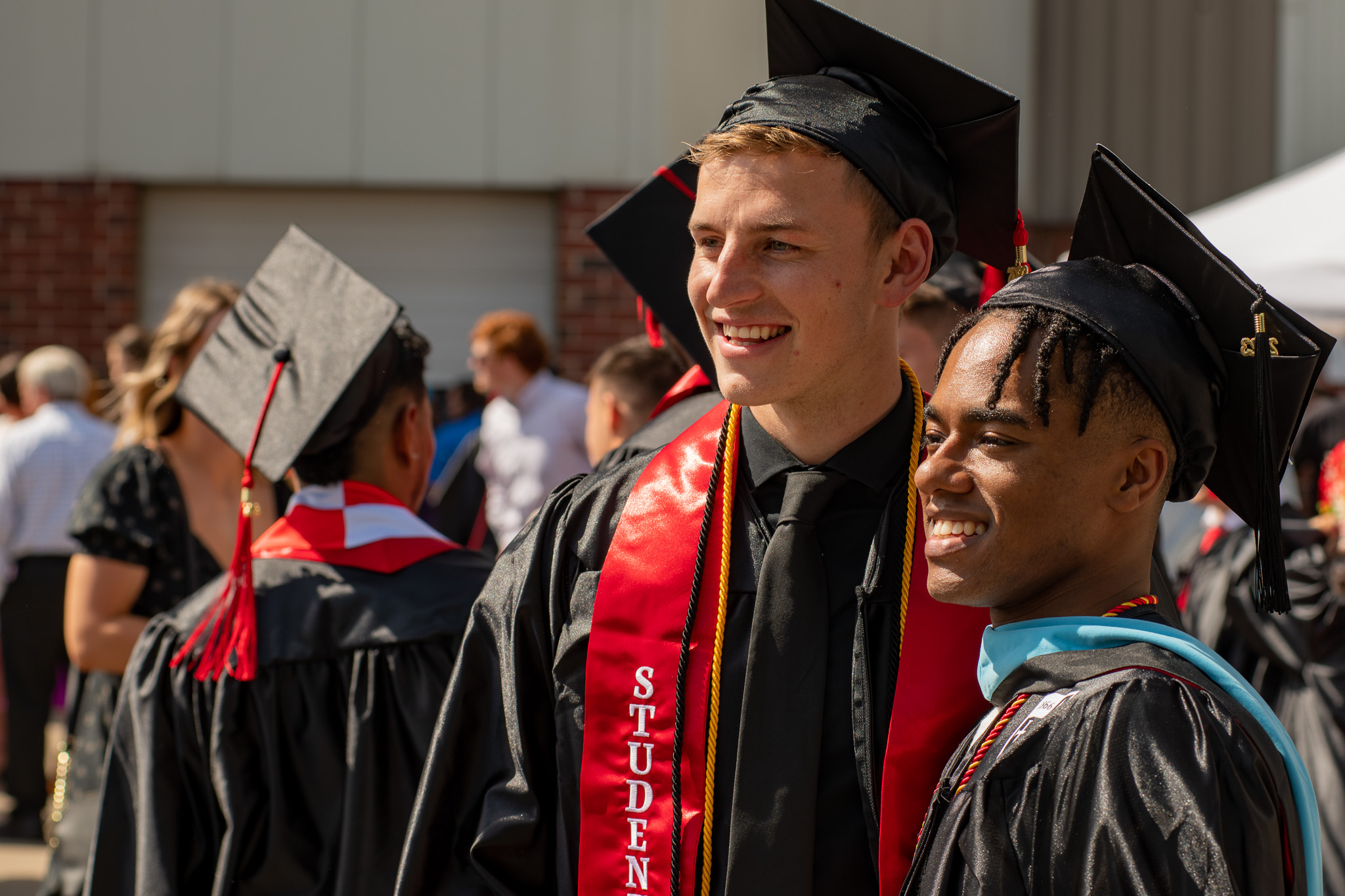 Roberts Wesleyan University graduates smile and pose for a photo at an outdoor commencement ceremony.