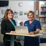 A nurse and nurse leader smile and stand together.