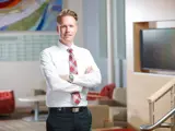 A business man wearing a white dress shirt, red plaid tie, and black trousers stands confidently with his arms crossed