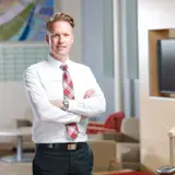 A business man wearing a white dress shirt, red plaid tie, and black trousers stands confidently with his arms crossed